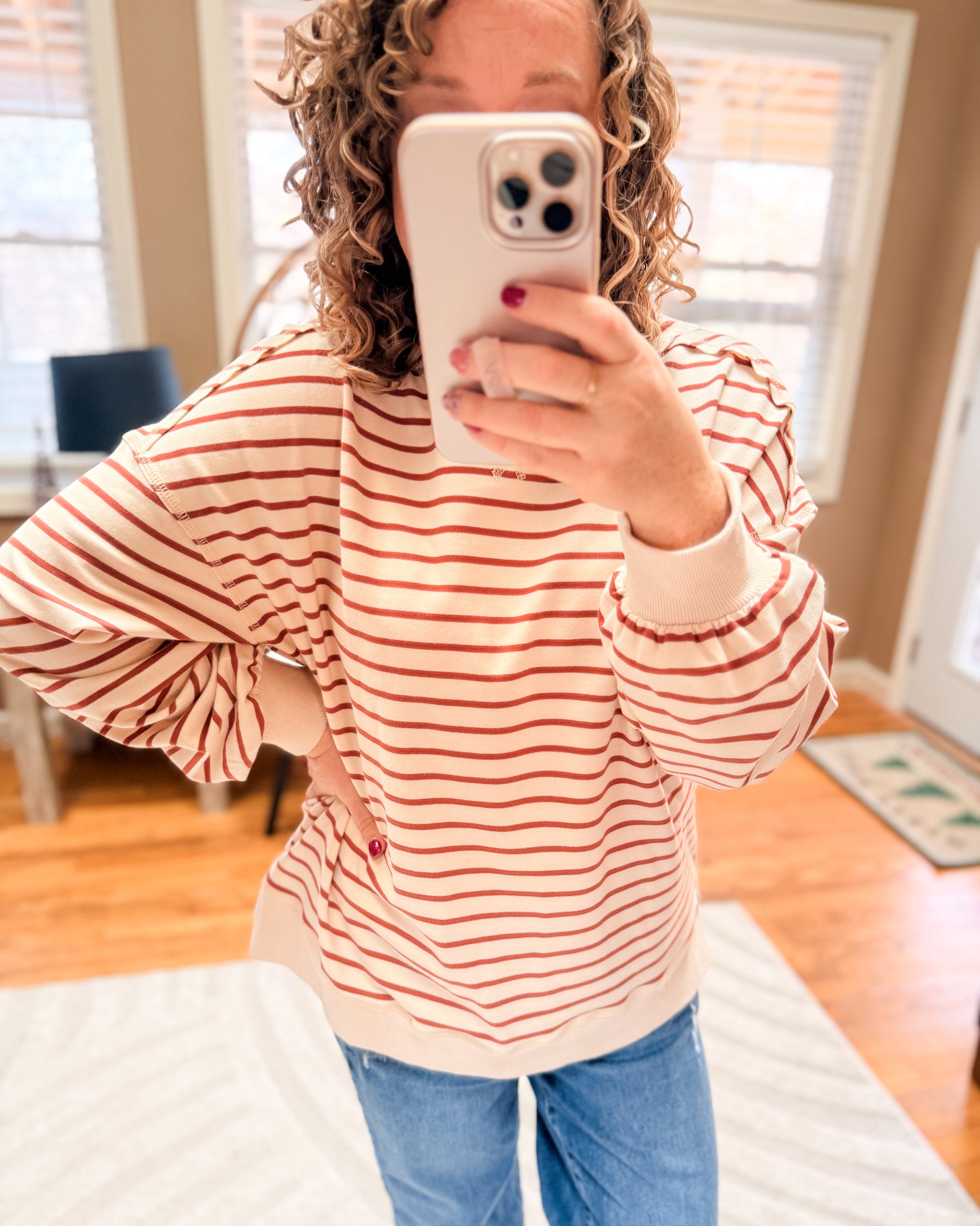Person wearing a red and white striped sweater and blue jeans, taking a mirror selfie.