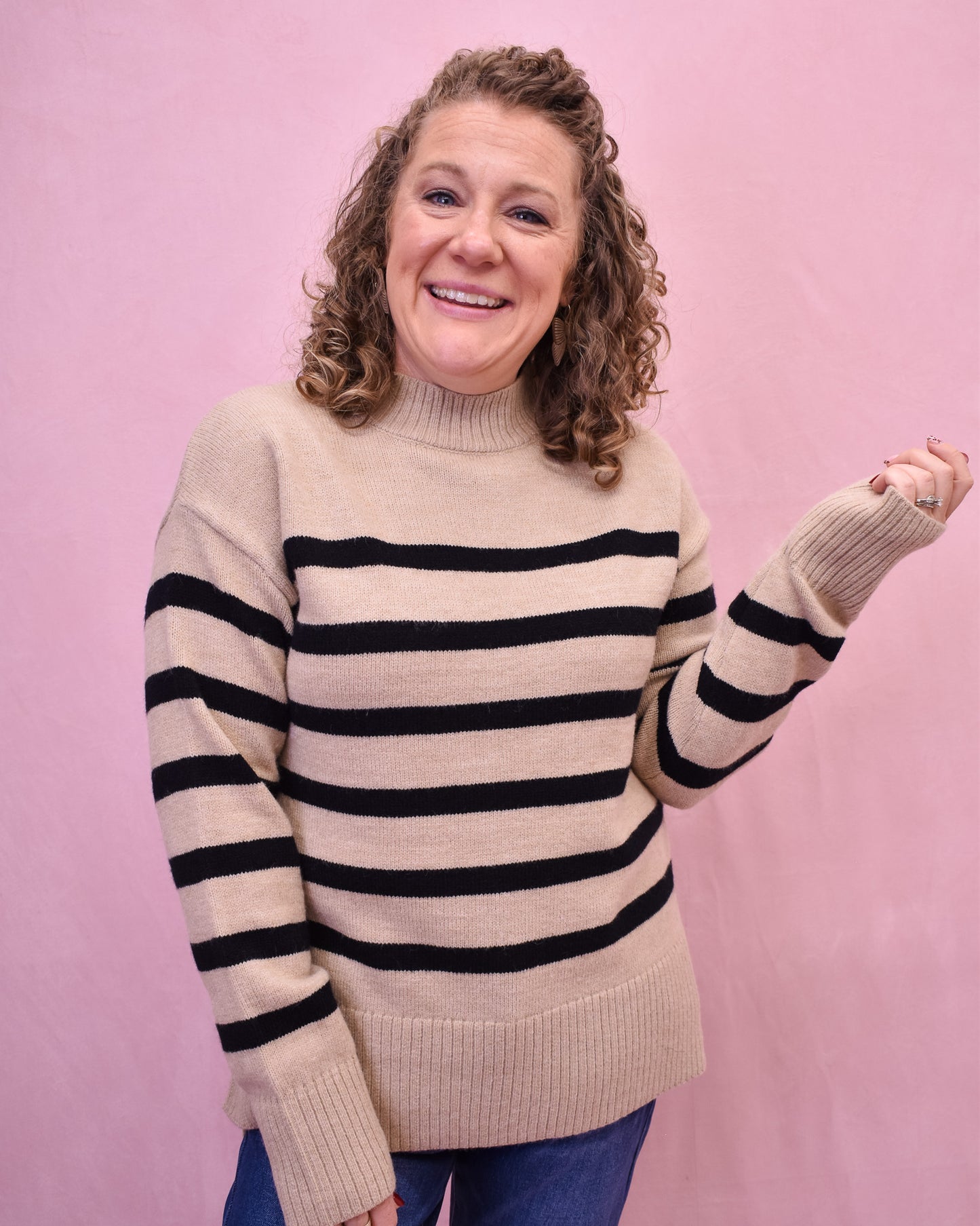 Person wearing a beige sweater with black stripes against a pink background