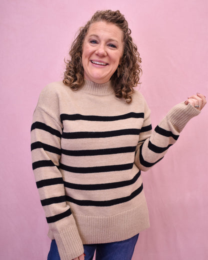 Person wearing a beige sweater with black stripes against a pink background