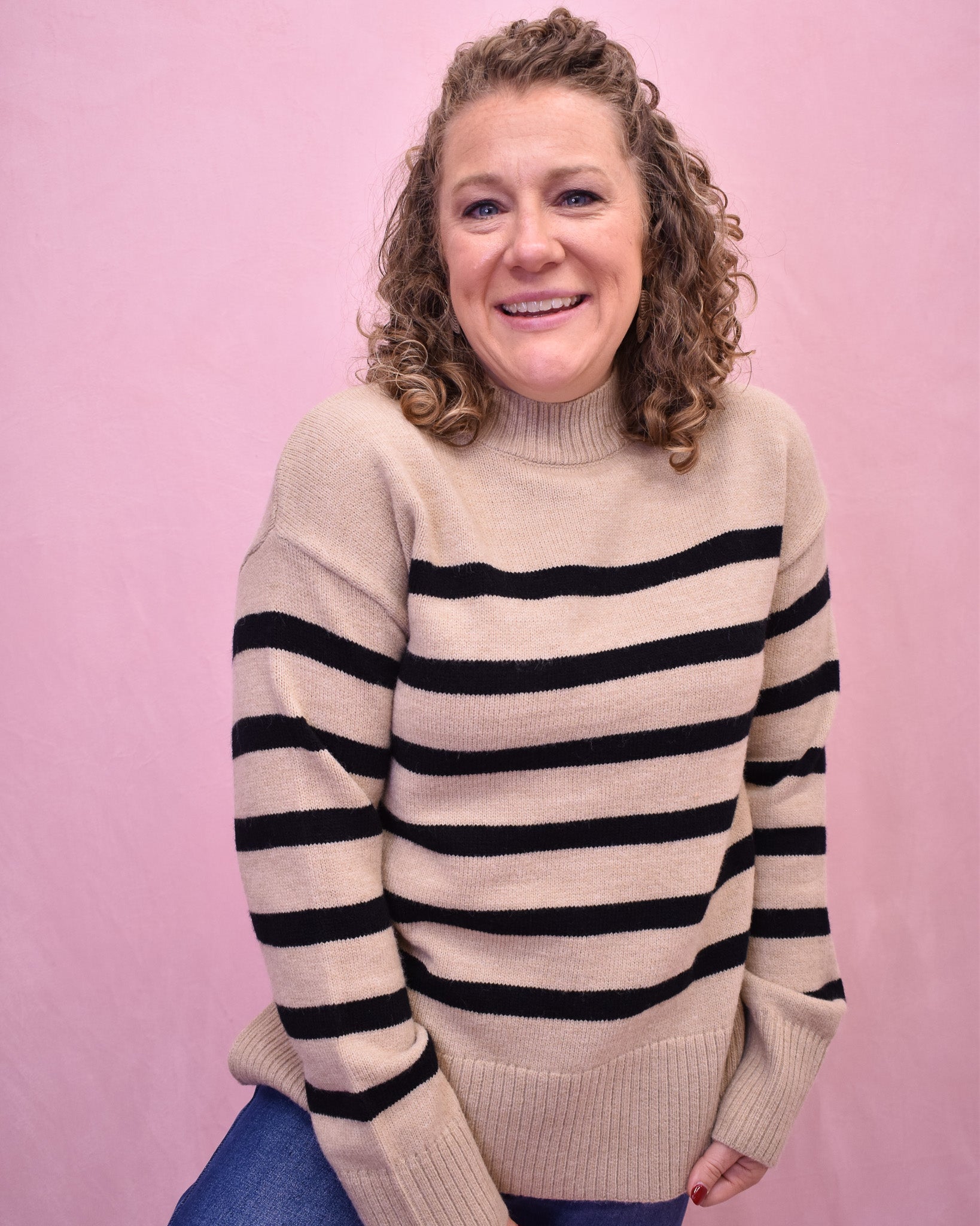 Woman wearing a beige sweater with black stripes against a pink background