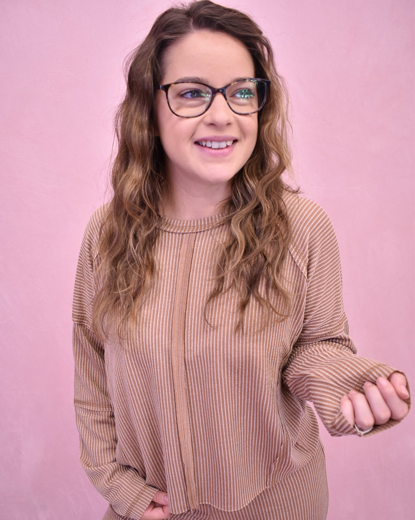 Woman wearing glasses and a brown ribbed sweater against a pink background