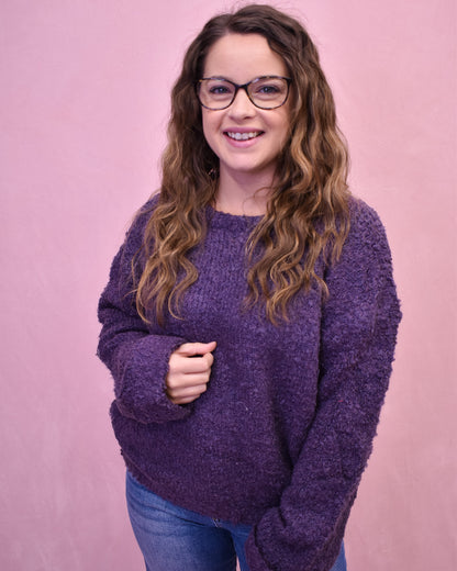 Woman wearing a purple sweater and glasses against a pink background