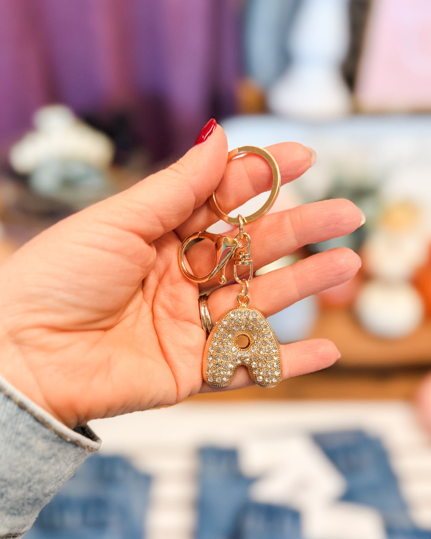 Hand holding a keychain with a decorative letter 'A' charm against a blurred indoor background
