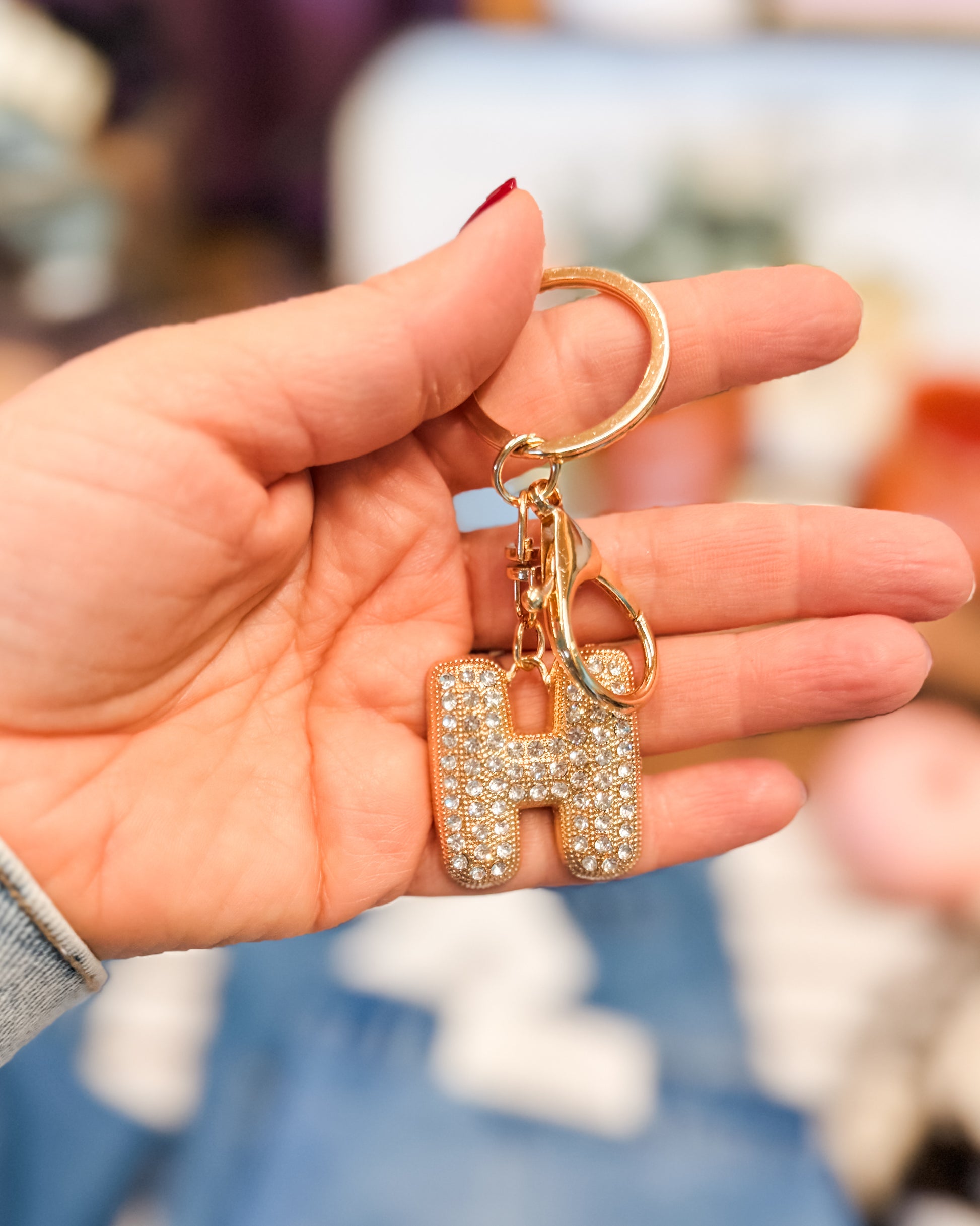 Hand holding a keychain with a letter 'H' charm against a blurred background