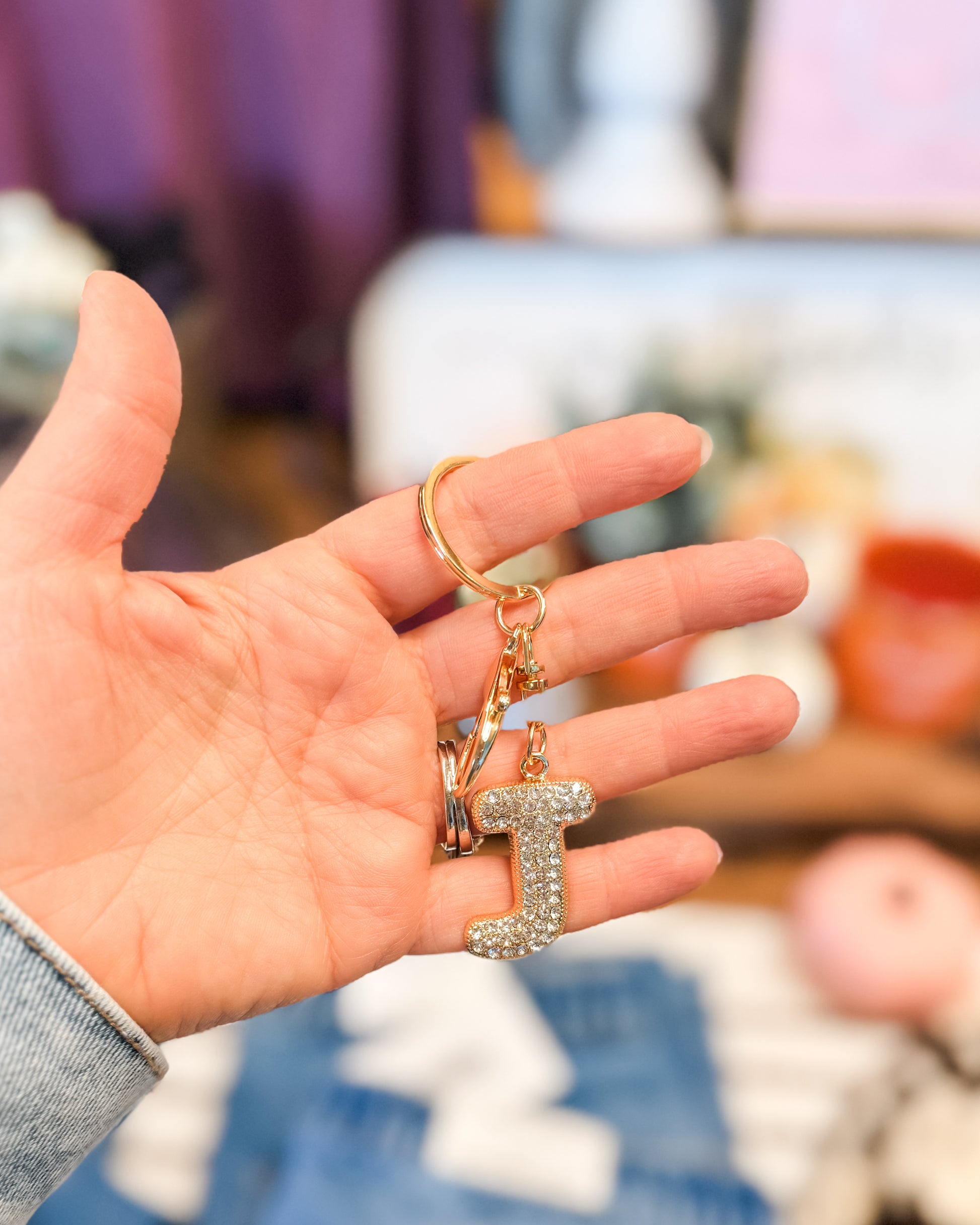 Hand holding a keychain with a letter 'I' charm against a blurred indoor background