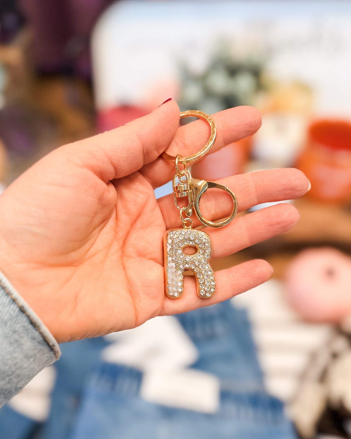 Hand holding a keychain with a letter 'R' charm against a blurred background