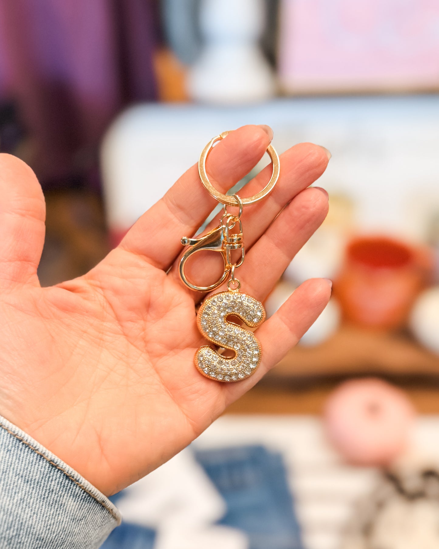 Hand holding a keychain with a letter 'S' design against a blurred indoor background