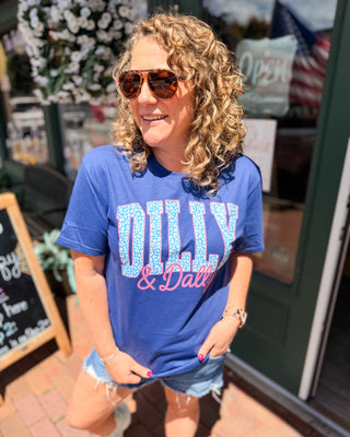 Woman wearing a blue t-shirt with 'Dilly Dally' text, standing outdoors.