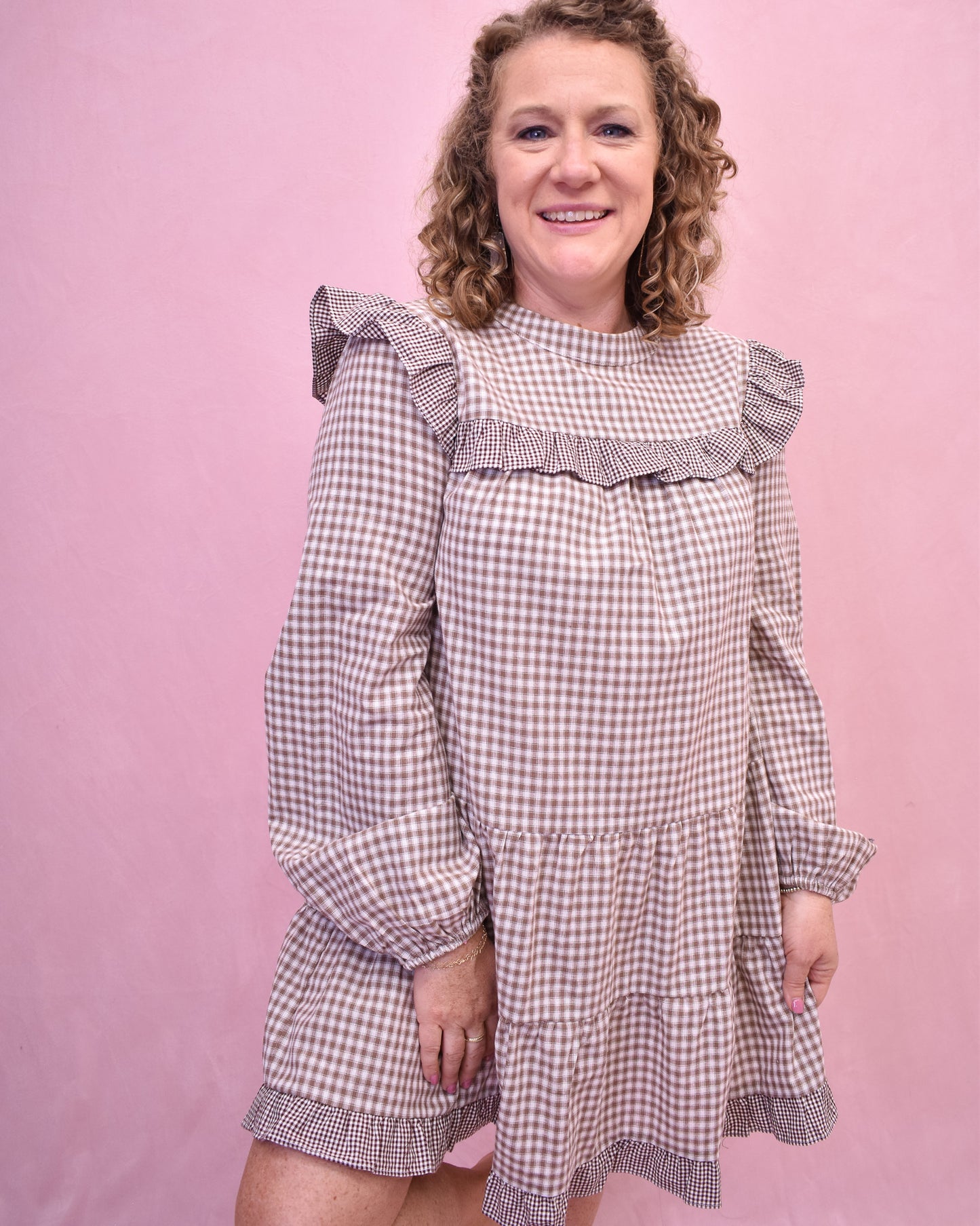 Woman wearing a checkered dress with ruffled details against a pink background