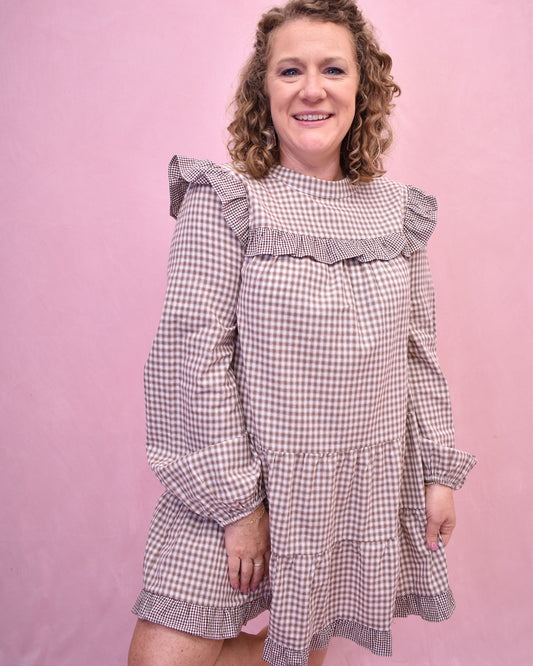 Woman wearing a checkered dress with ruffled details against a pink background