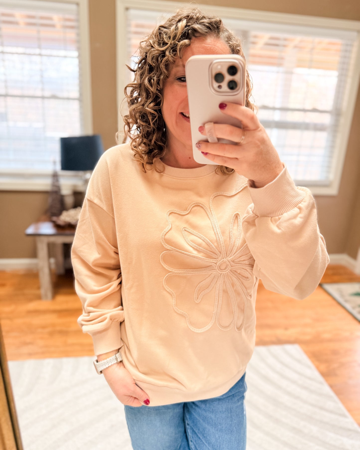 Person wearing a beige sweater with a floral design in a room.