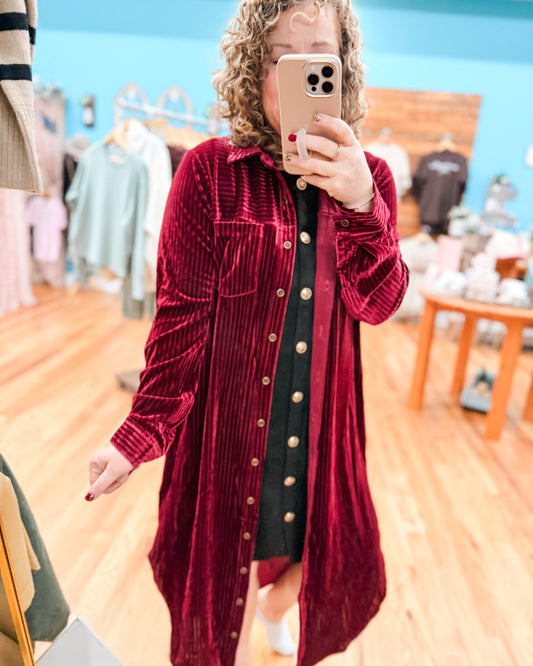 Person wearing a red velvet dress with gold buttons in a store setting.
