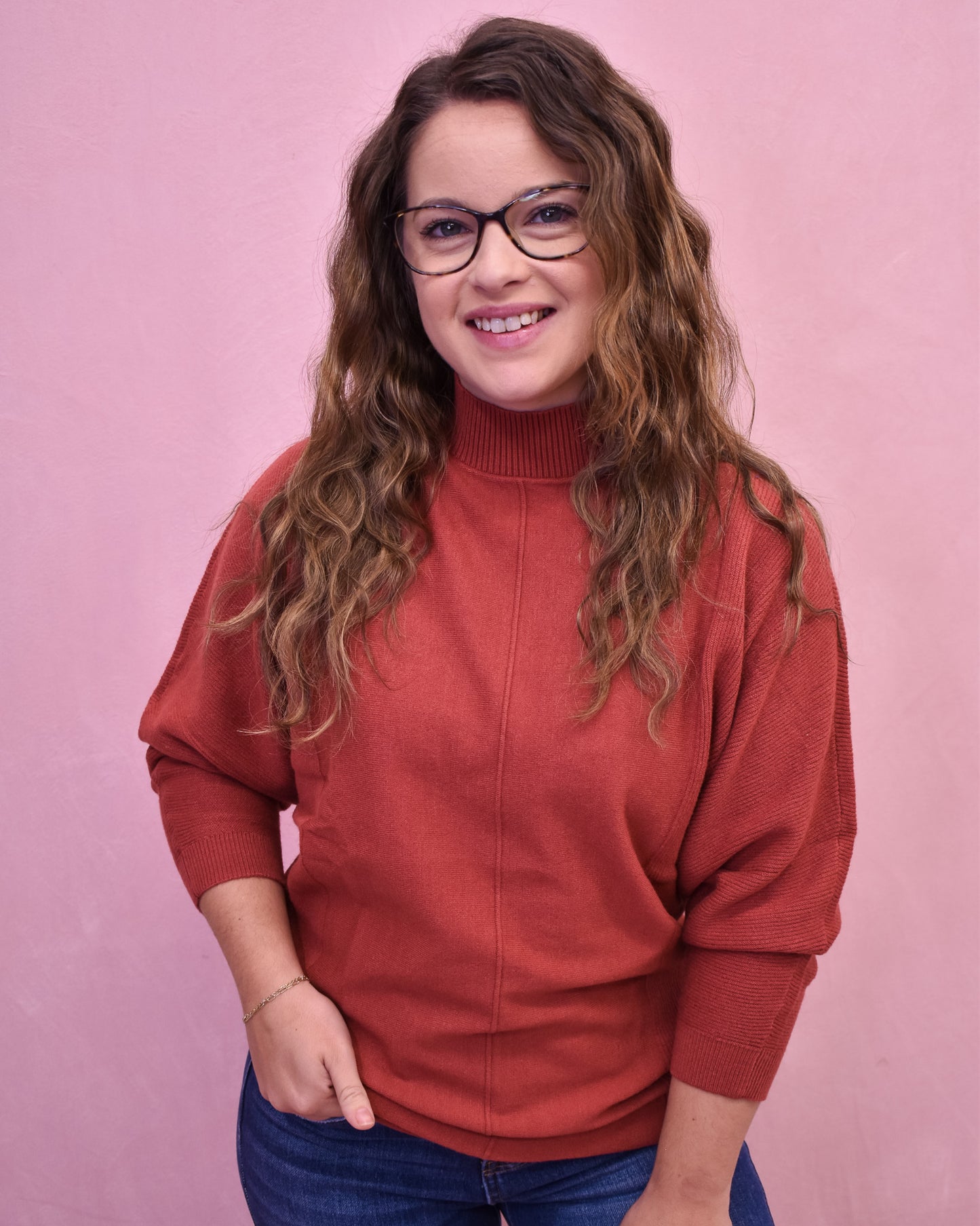 Woman wearing a red sweater and glasses against a pink background