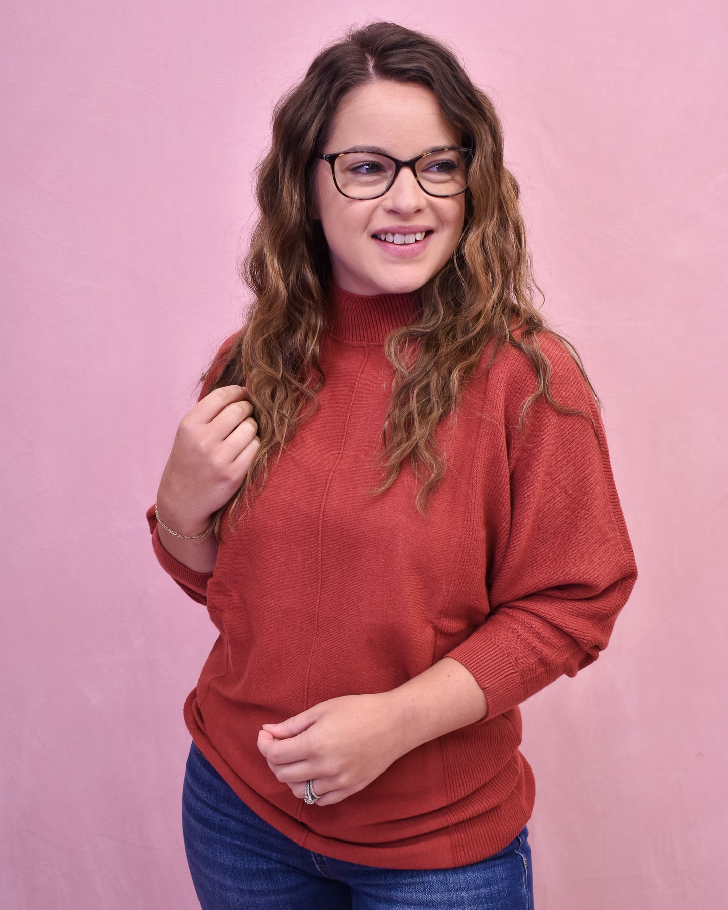 Woman wearing a red sweater and glasses against a pink background