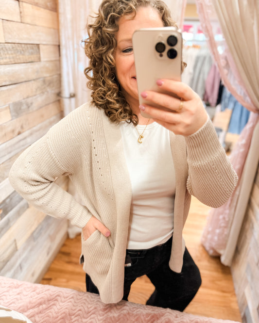 Person wearing a beige cardigan taking a mirror selfie in a store.