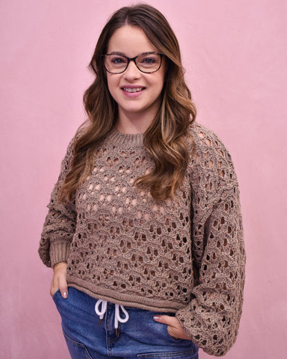 Woman wearing a brown crochet sweater against a pink background