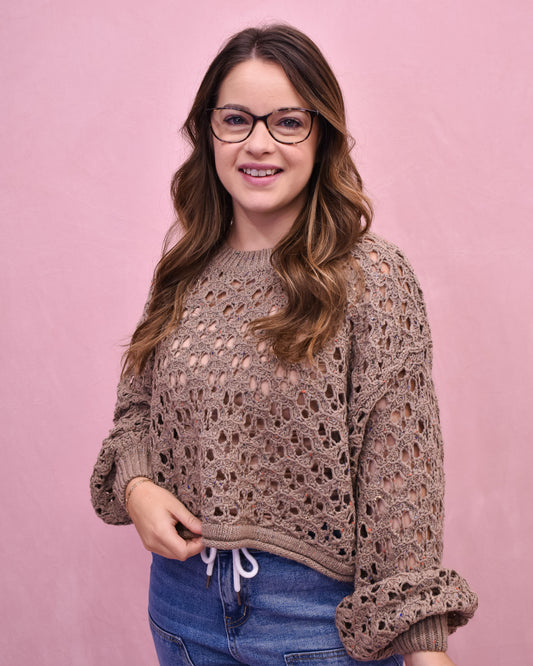Woman wearing a brown crochet sweater against a pink background