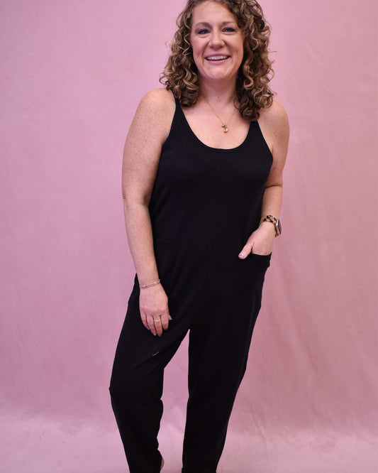 Woman wearing a black sleeveless top and pants against a pink background