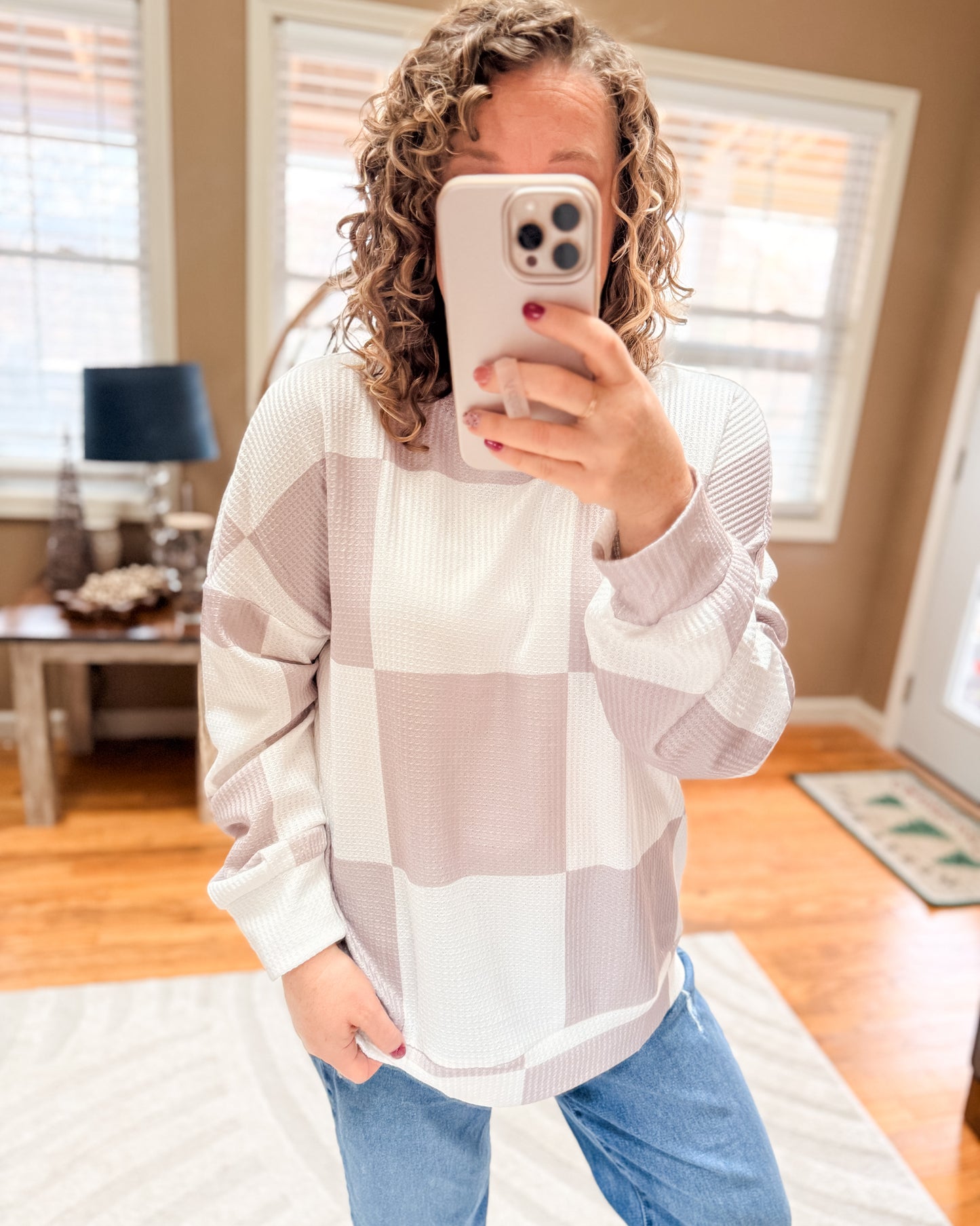 Person wearing a checkered sweater and blue jeans taking a mirror selfie.