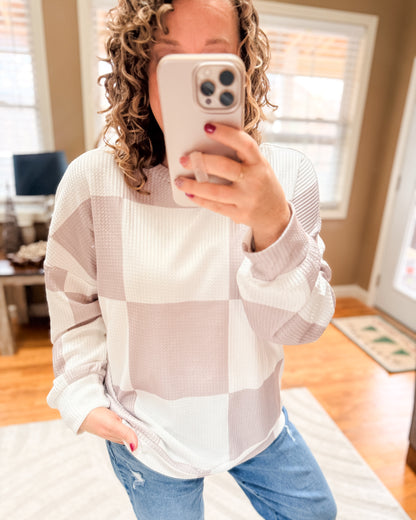 Person wearing a checkered sweater and jeans, taking a mirror selfie.