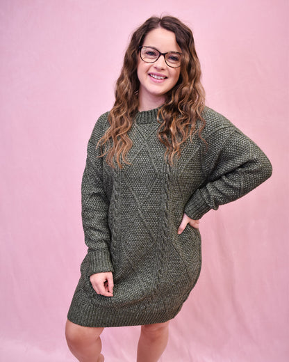 Woman wearing a green cable knit sweater dress against a pink background