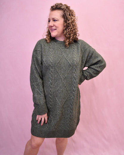 Woman wearing a green cable knit sweater dress against a pink background