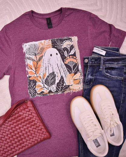 Purple t-shirt with ghost design, jeans, white sneakers, and red clutch on a light background