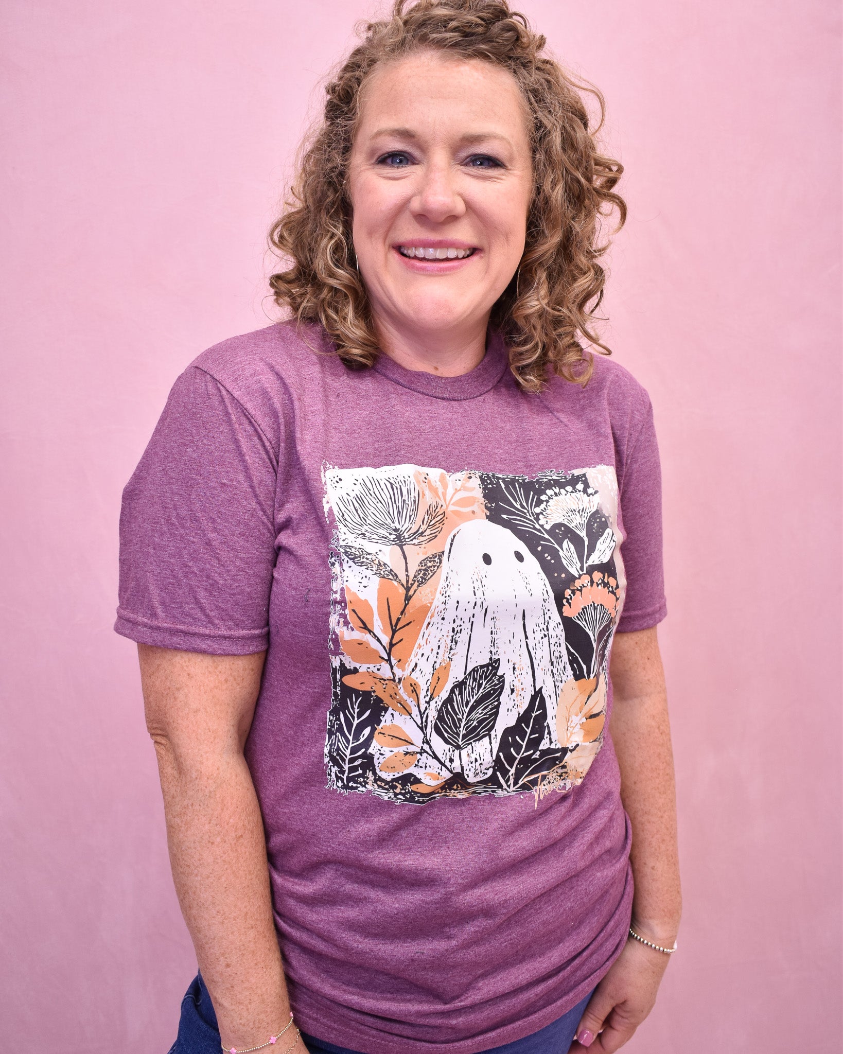Woman wearing a purple t-shirt with a white bear and leaf design on a pink background