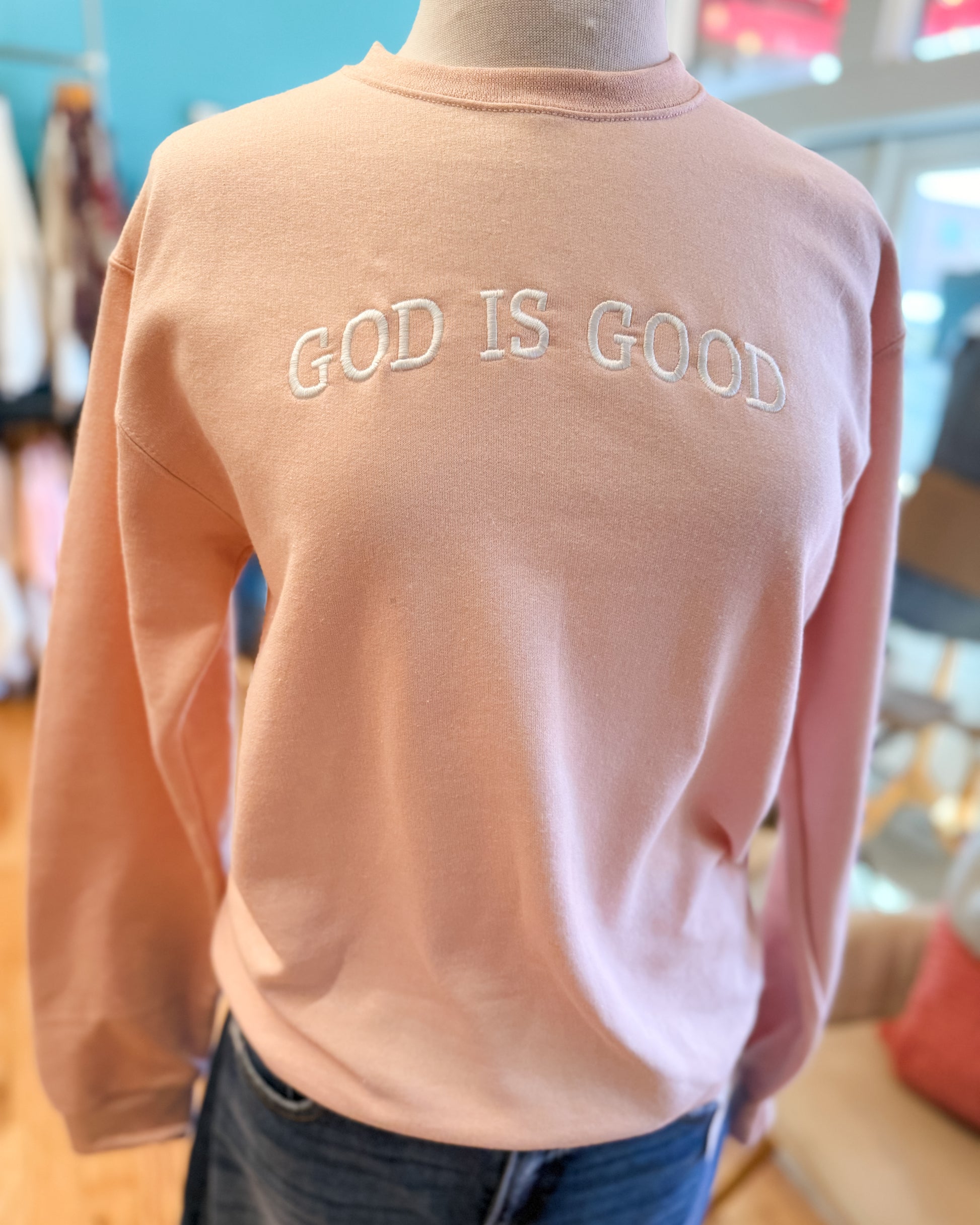 Person wearing a pink sweatshirt with 'GOD IS GOOD' text in a casual setting.