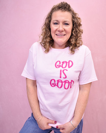 Woman wearing a white t-shirt with 'GOD IS GOOD' in pink text against a pink background