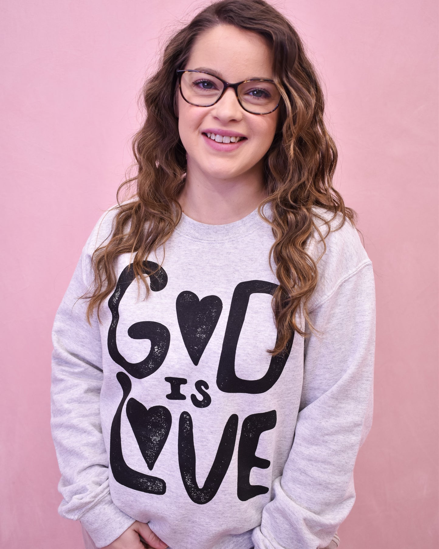 Person wearing a sweatshirt with 'God is Love' text on a pink background