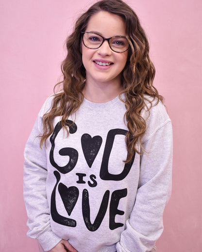 Person wearing a sweatshirt with 'God is Love' text on a pink background