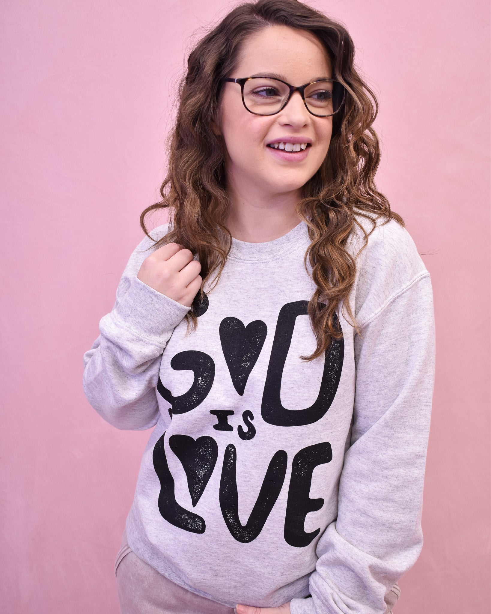 Person wearing a gray sweatshirt with 'God is Love' text on a pink background