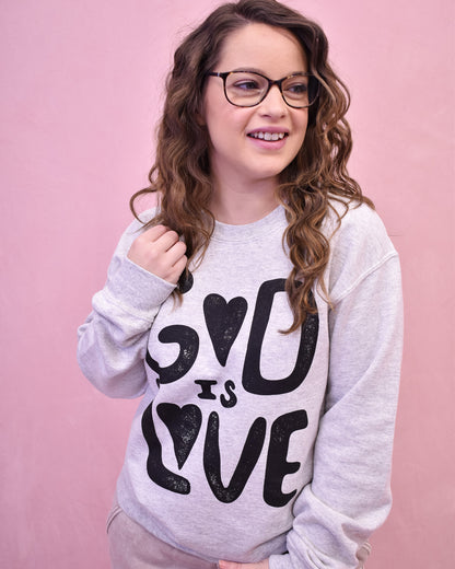 Person wearing a gray sweatshirt with 'God is Love' text on a pink background