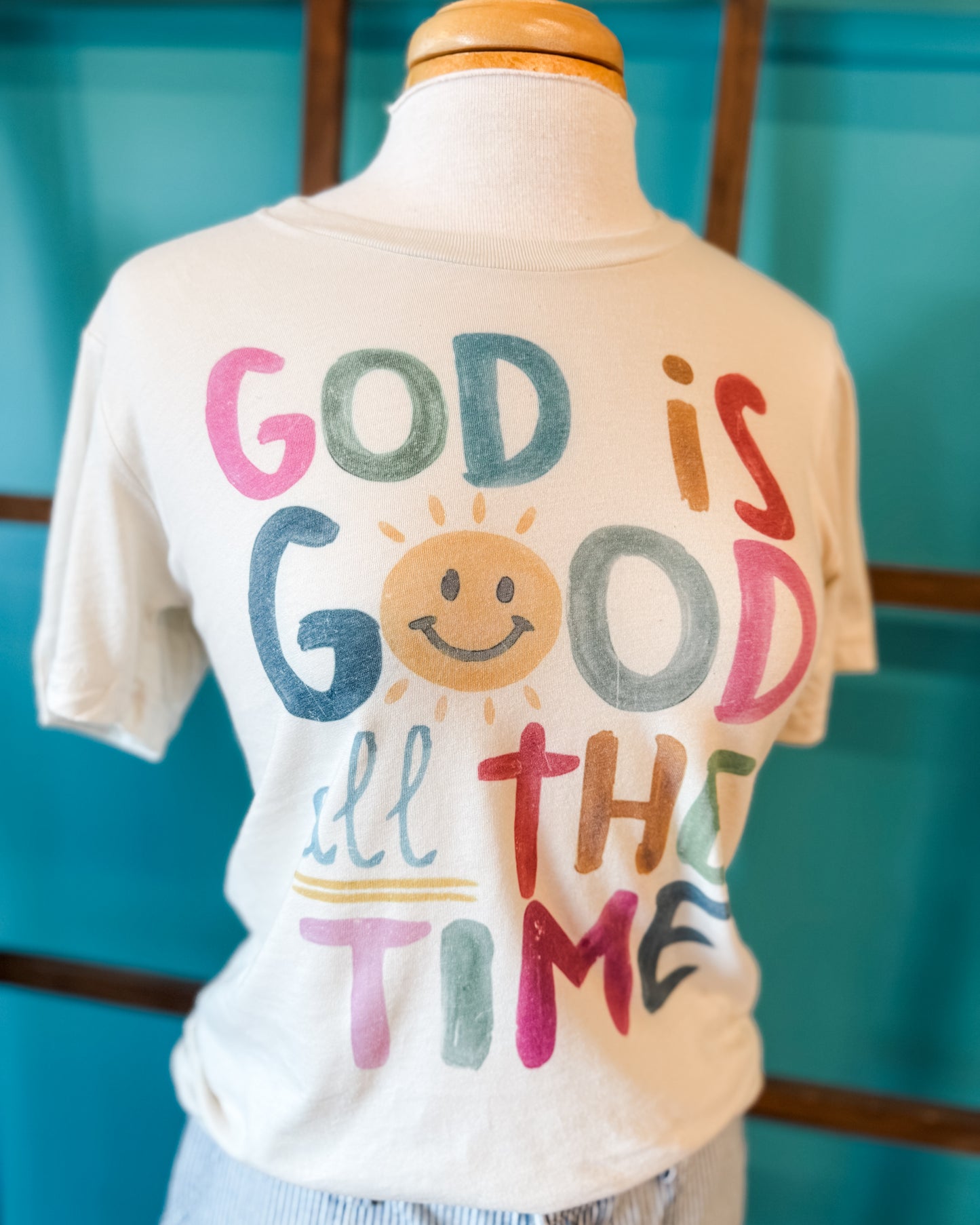 T-shirt with 'God is Good All The Time' text on a mannequin against a blue background
