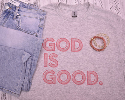 Gray t-shirt with 'GOD IS GOOD.' text, blue jeans, and a bracelet on a white lace background