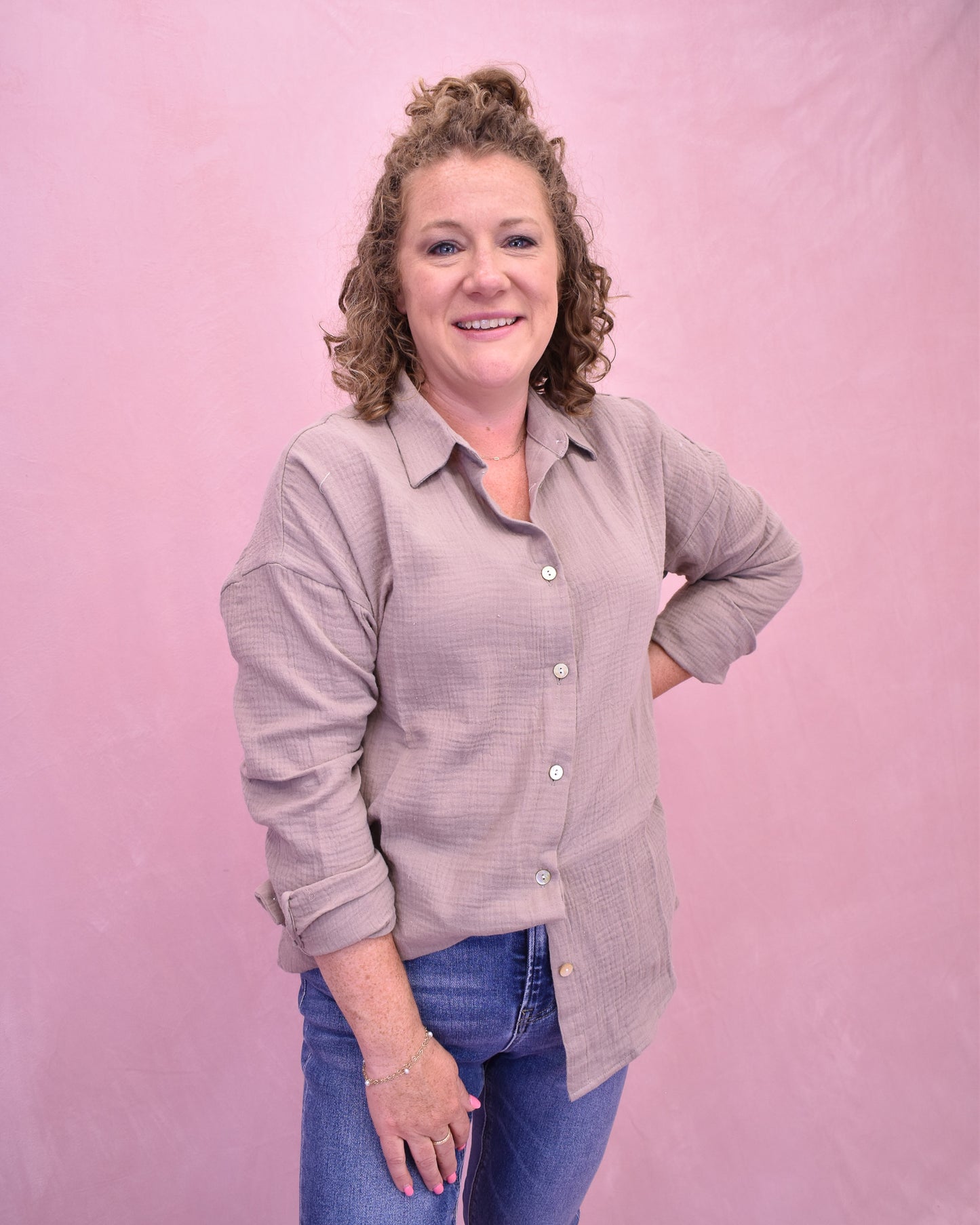 Woman wearing a light purple button-up shirt and blue jeans against a pink background