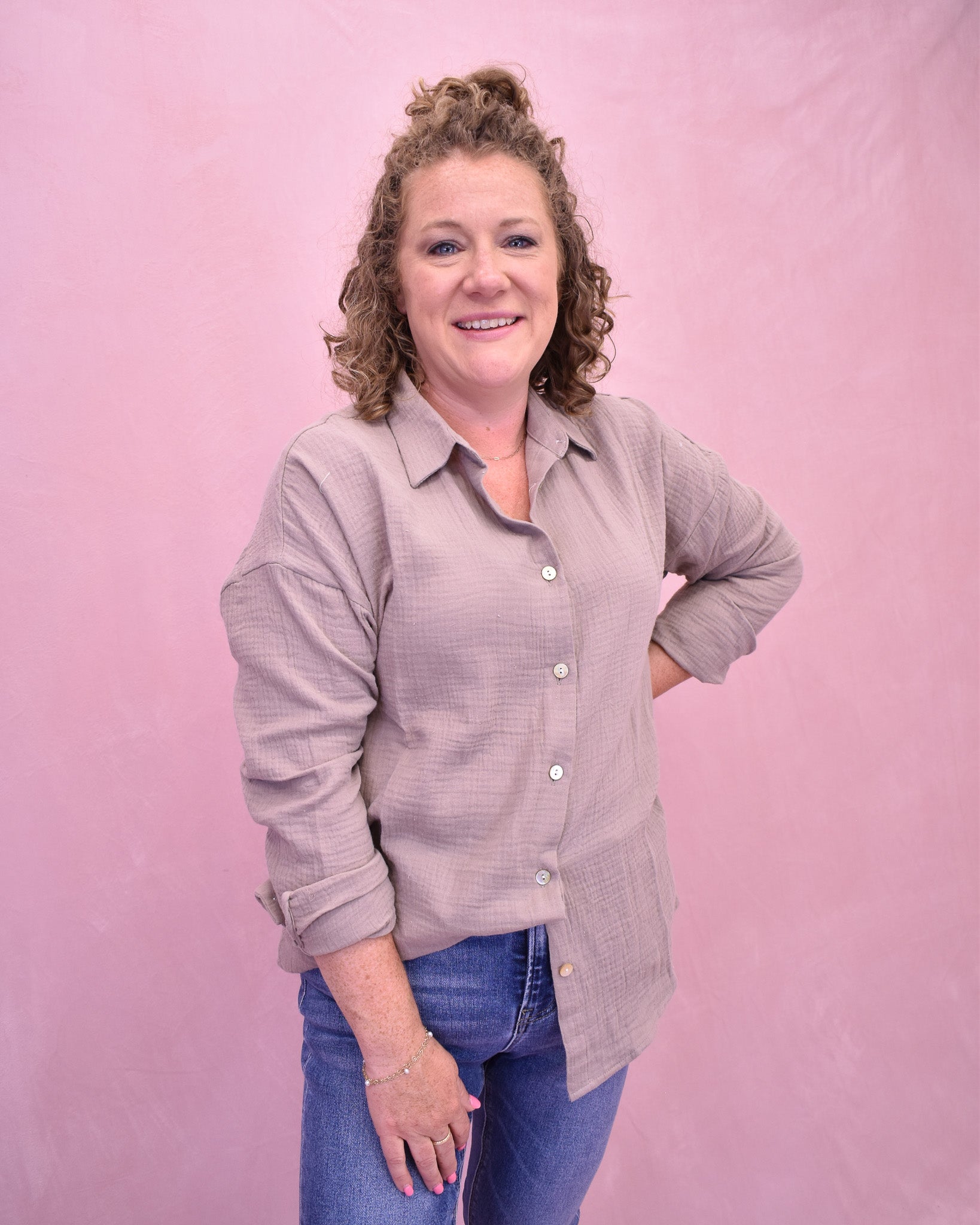 Woman wearing a light purple button-up shirt and blue jeans against a pink background