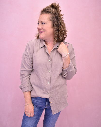 Woman wearing a light gray button-up shirt and blue jeans against a pink background