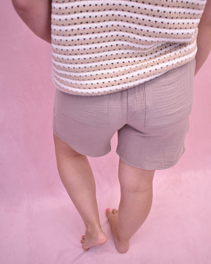 Person wearing a striped shirt and light purple shorts on a pink background