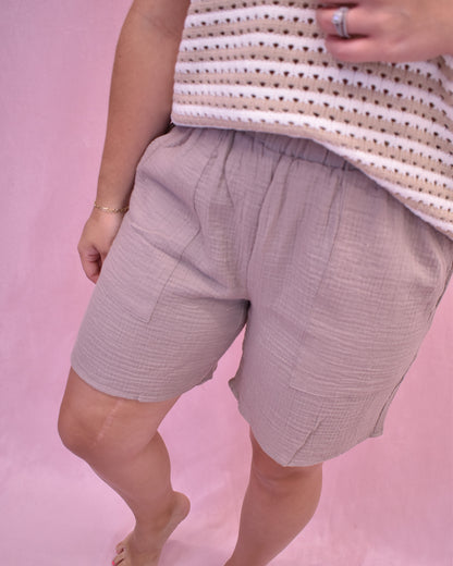 Person wearing light purple shorts and a striped shirt on a pink background