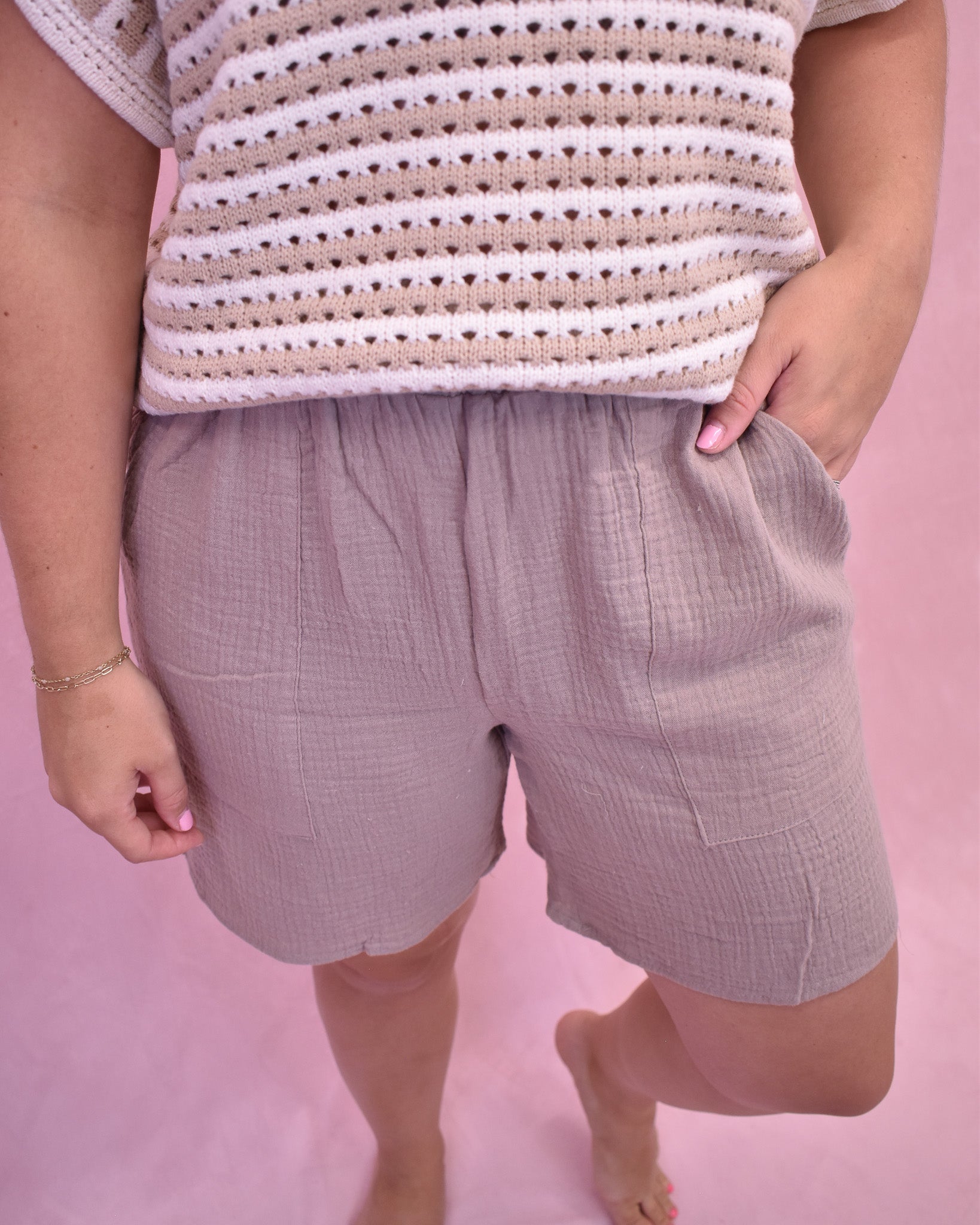 Person wearing a striped shirt and checkered shorts on a pink background