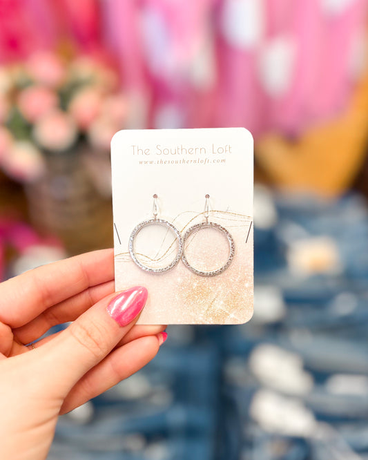 Hand holding a card with silver earrings on a blurred floral background