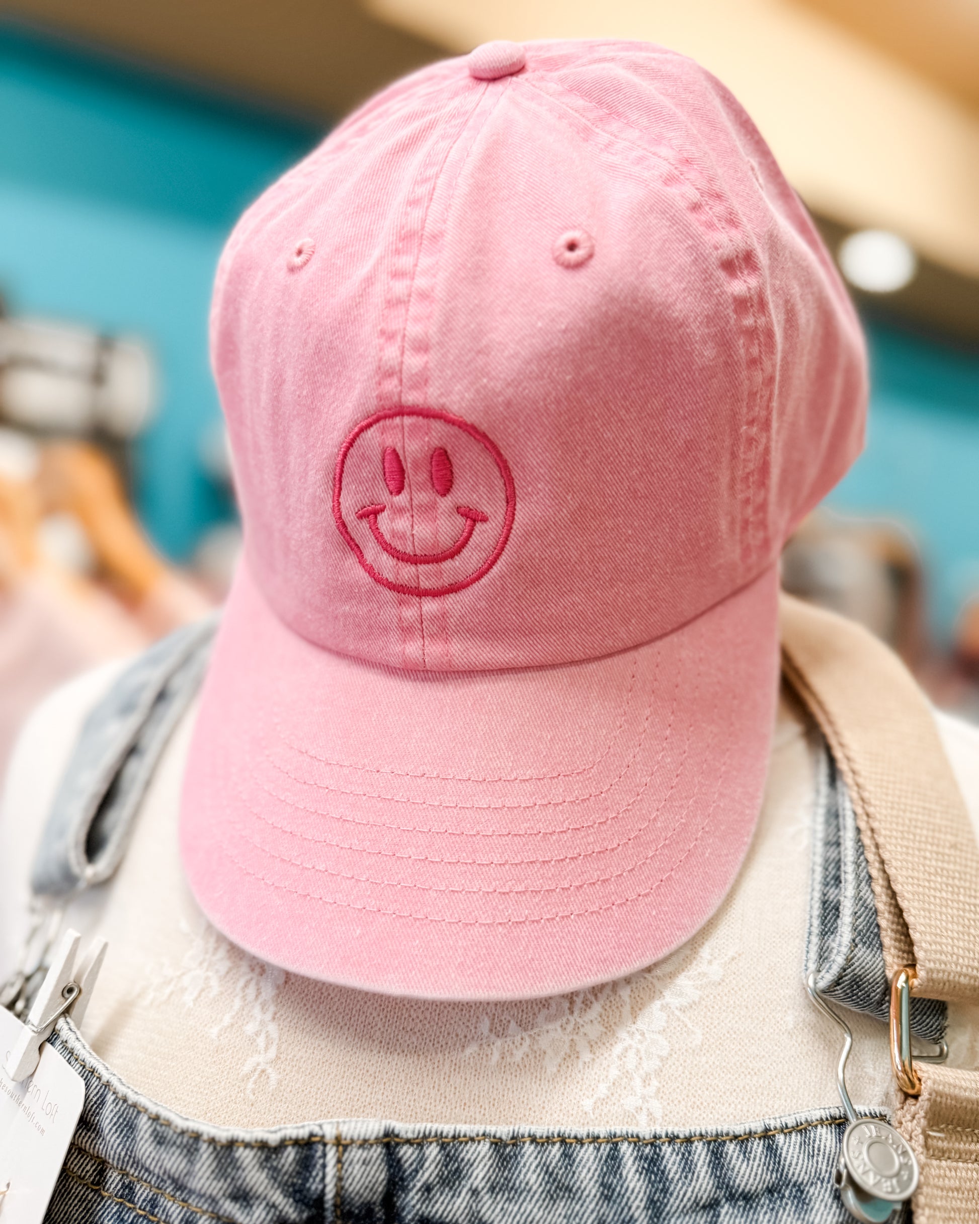 Pink cap with a smiley face design worn by a person in an indoor setting.