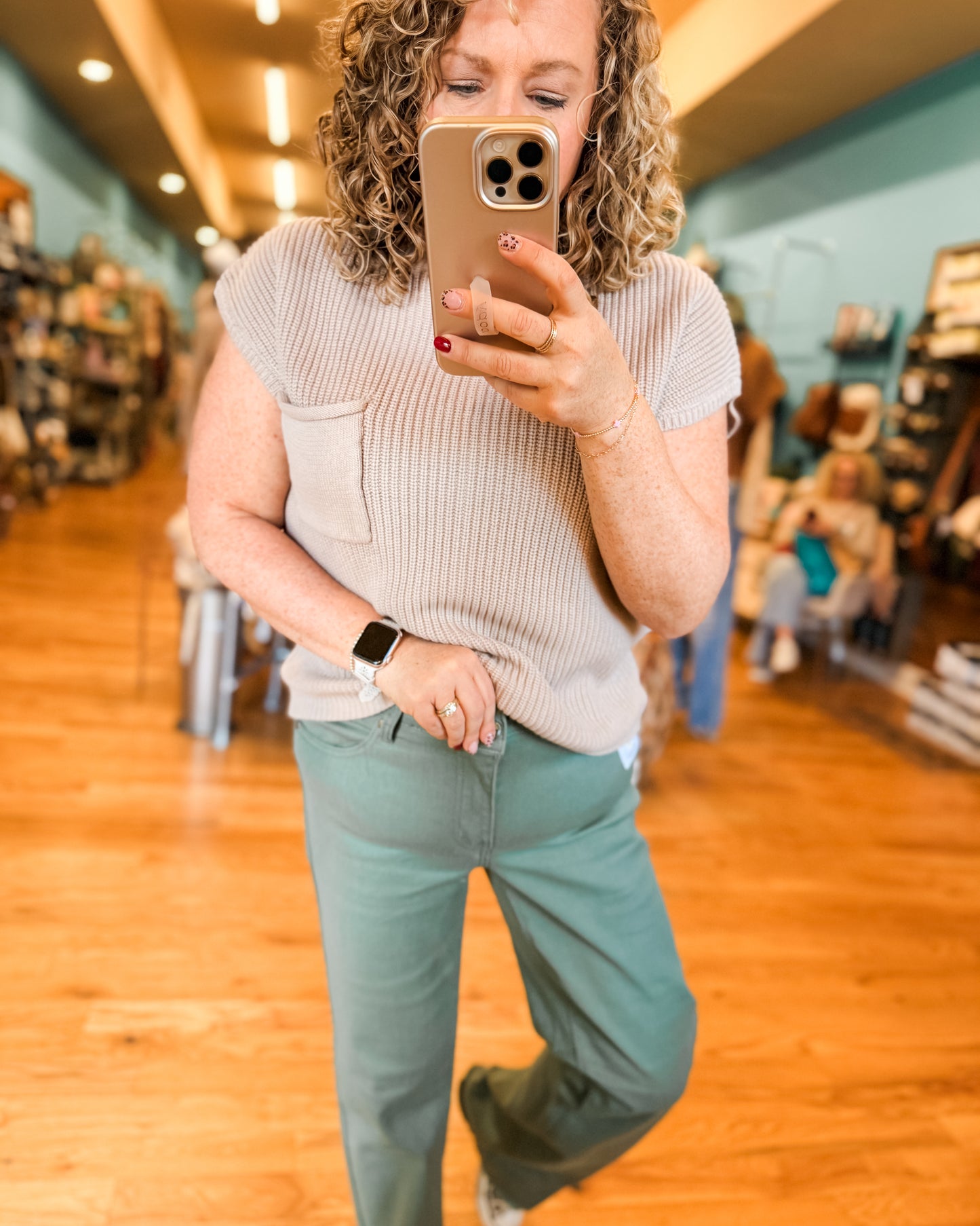 Woman taking a mirror selfie in a store, wearing a beige top and light blue pants.