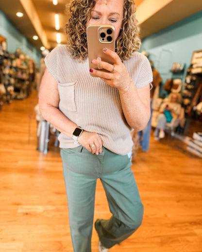 Woman taking a mirror selfie in a store, wearing a beige top and light blue pants.