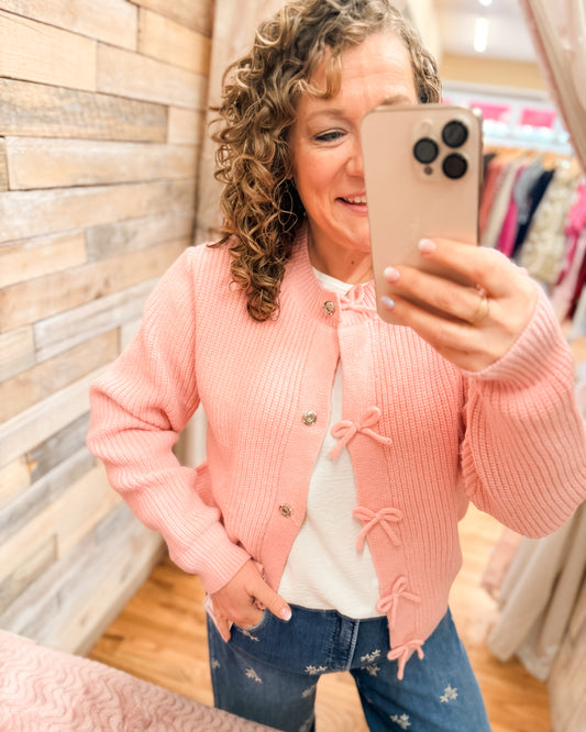 Pink bow sweater cardigan paired with a lightweight white top and embroidered floral jeans.