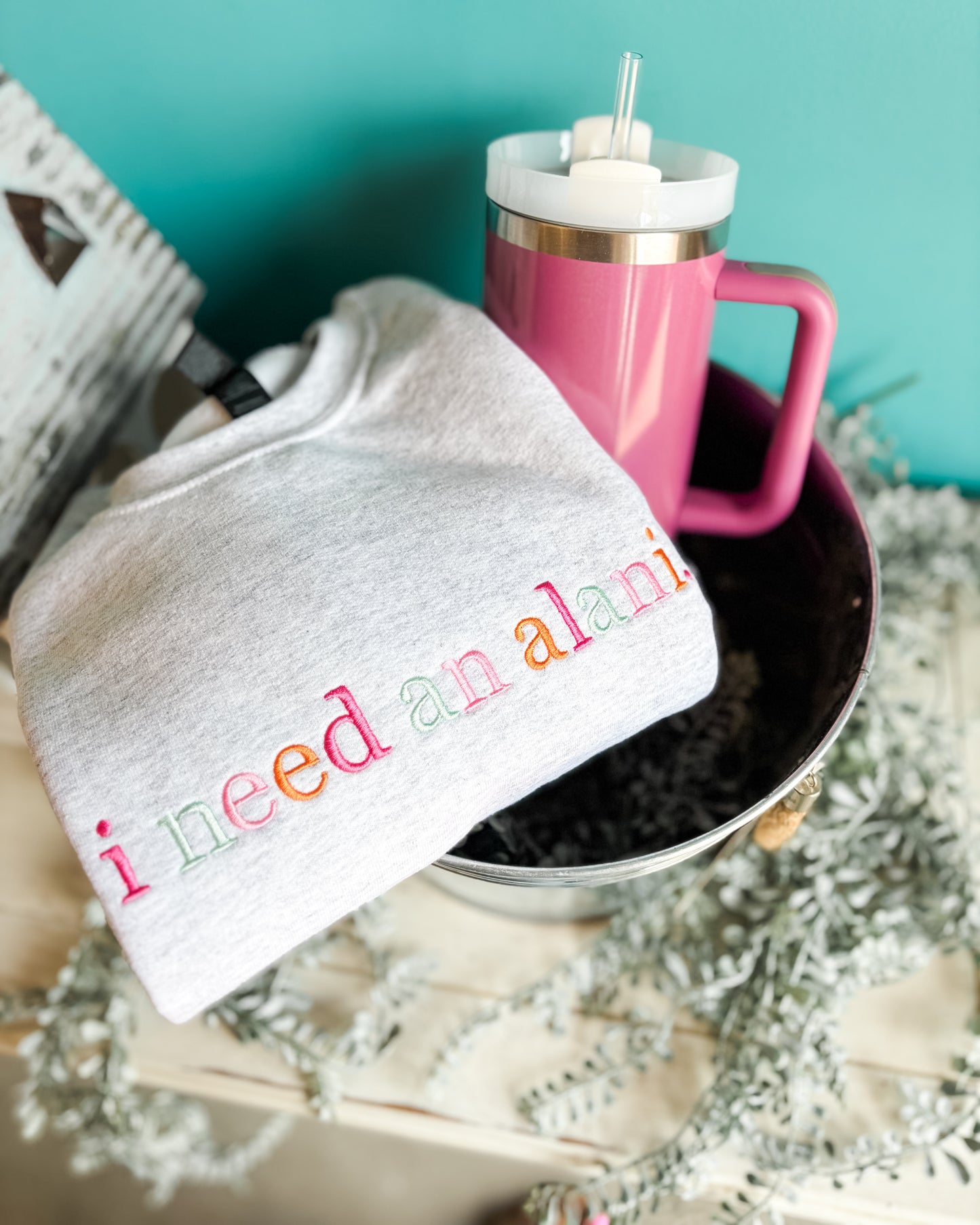 Gray sweatshirt with colorful text, pink mug, and straw on a decorative surface.