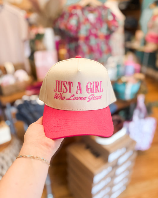 Beige and red cap with 'Just a Girl Who Loves Jesus' text held in a store setting.