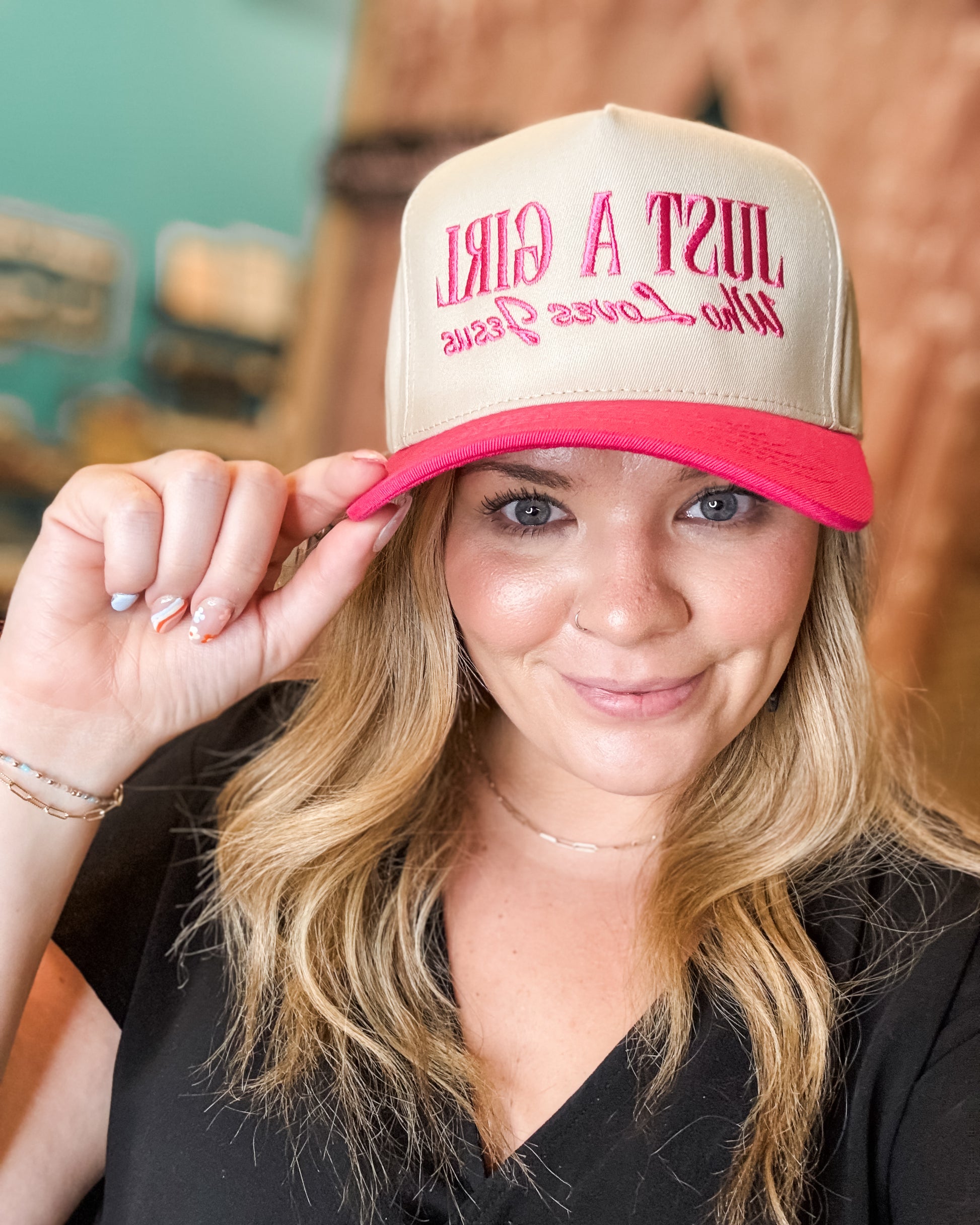Woman wearing a beige and pink cap with text, indoors.